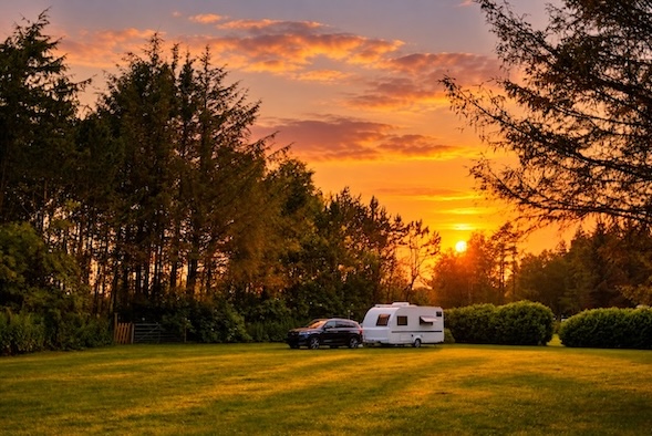 Caravan and towing vehicle parked in a meadow at sunset
